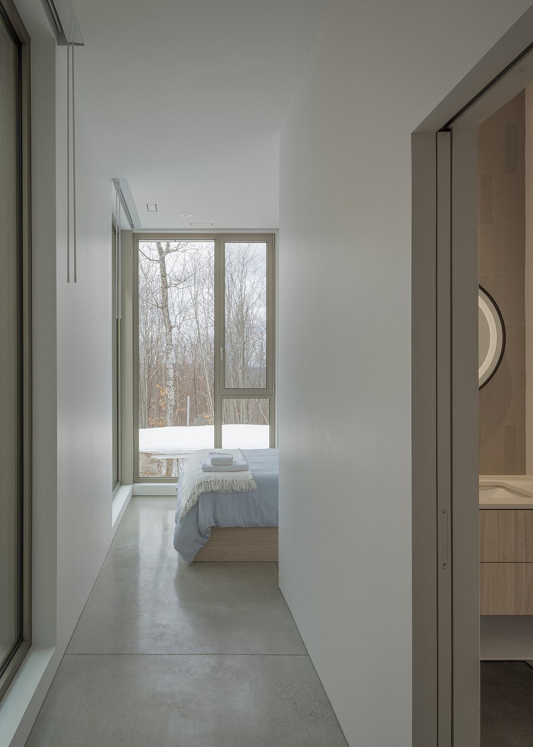 Minimalist bedroom with large windows overlooking a snowy forest landscape.