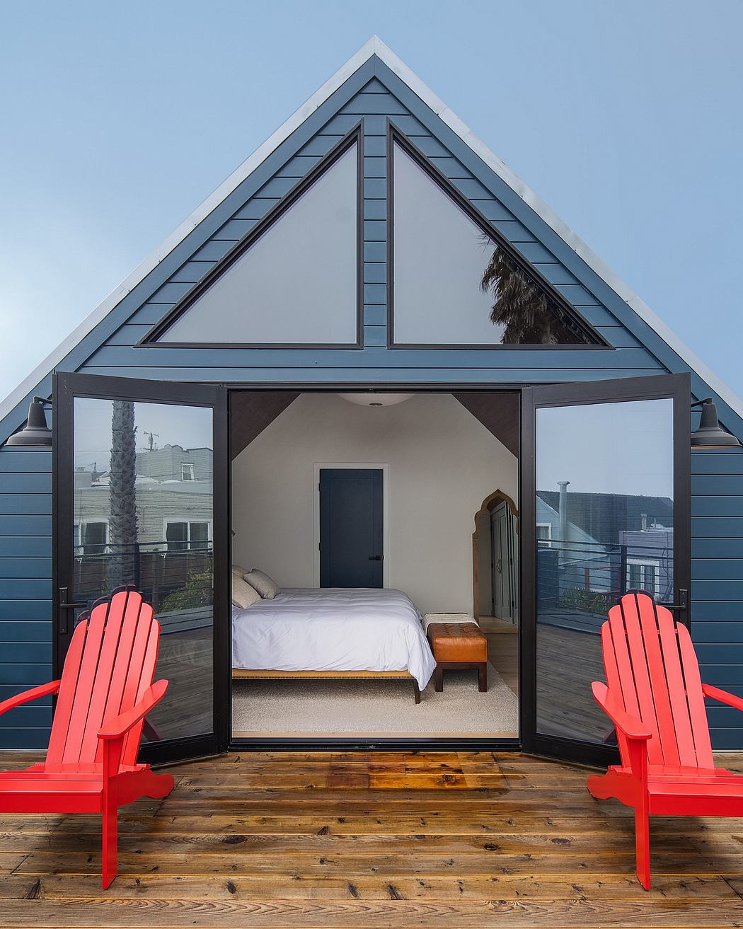 A modern A-frame cabin with sleek black trim, floor-to-ceiling windows, and cozy Adirondack chairs on the deck.