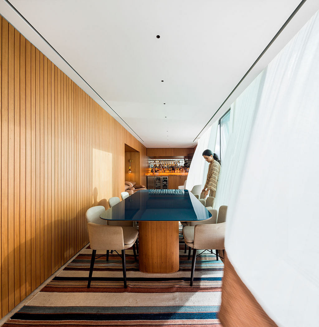 Warm wooden walls, modern sleek table, plush chairs, and patterned carpet create a cozy atmosphere.