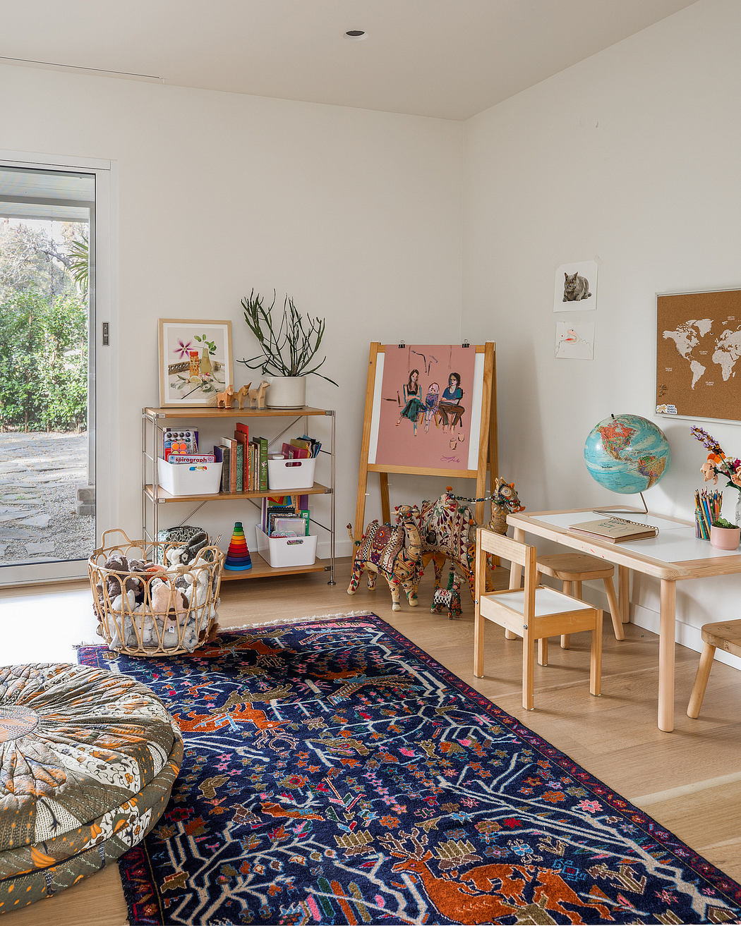 A bright, eclectic room with a colorful patterned rug, shelving, and artistic decor.