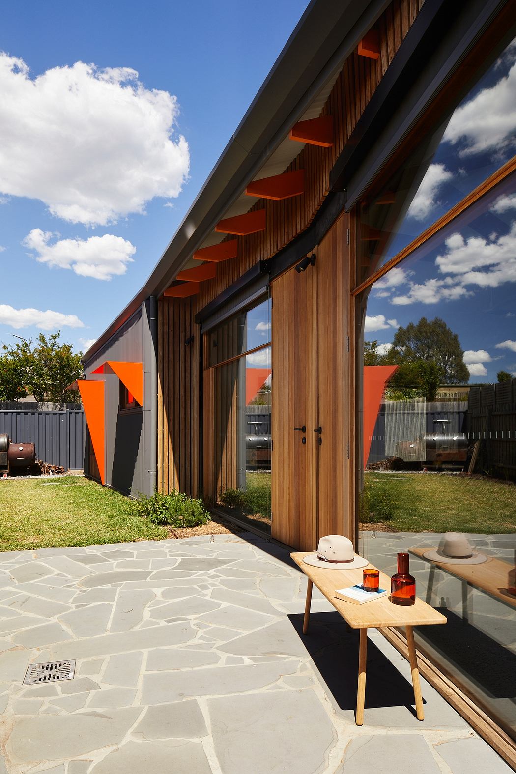 Wooden structure with orange accents and paved courtyard, featuring rustic furniture.