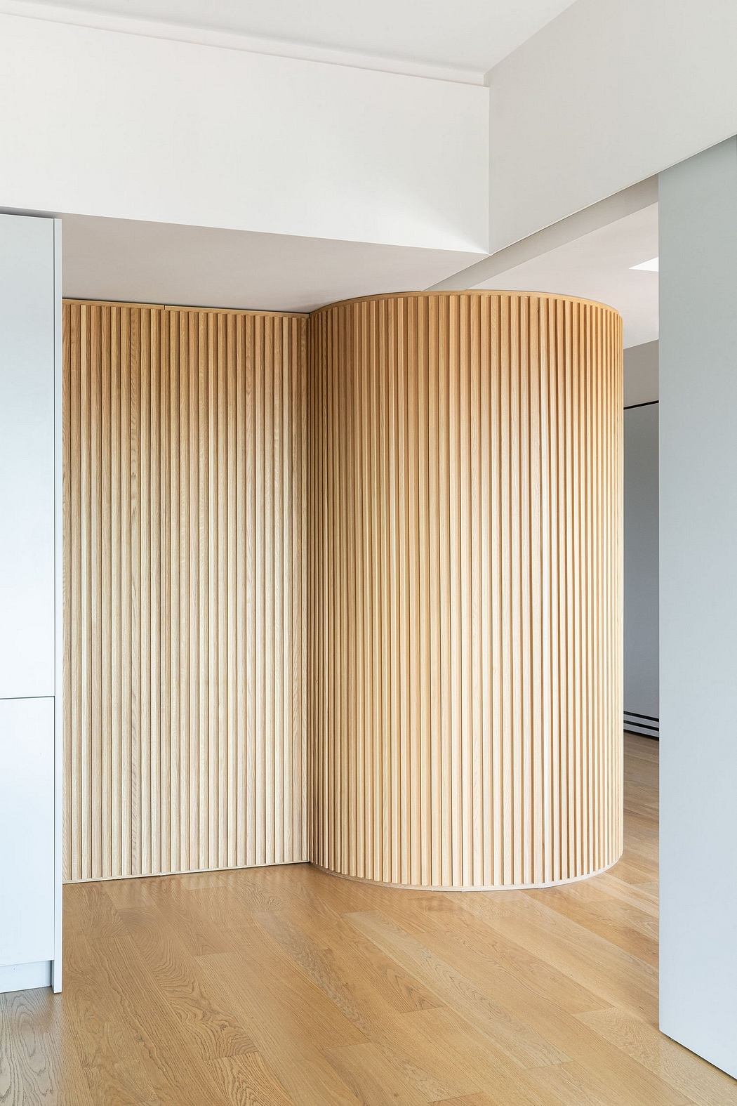 Cylindrical wooden wall panels with vertical striations in a minimalist room.