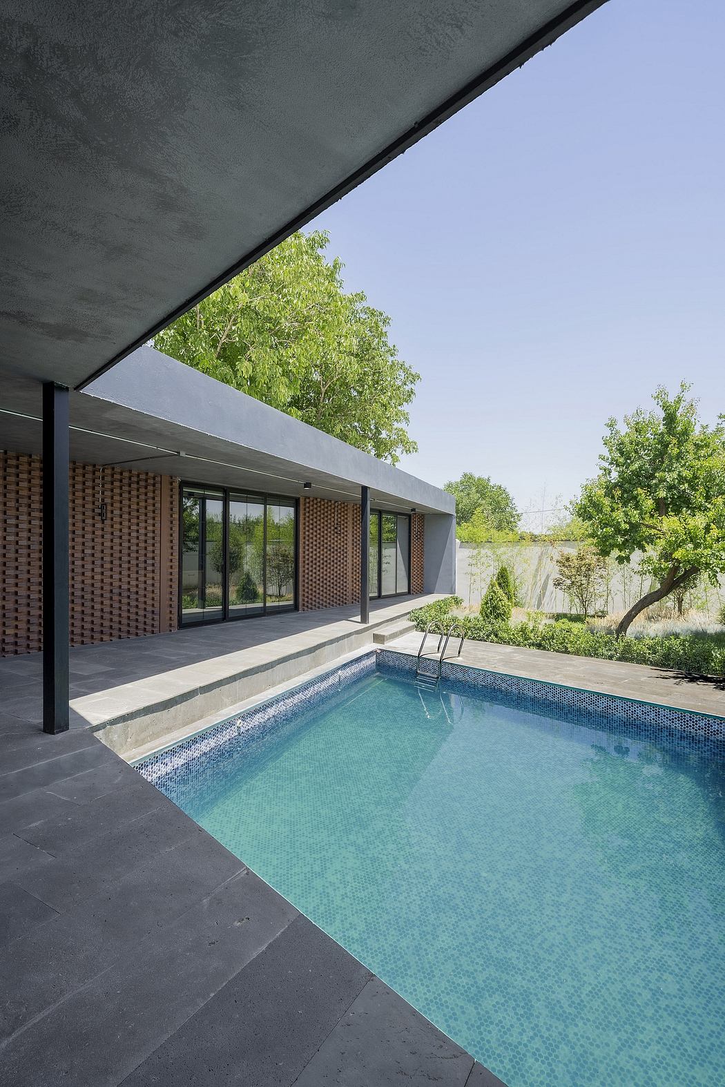 Sleek, modern pool house with brick and glass facade, surrounded by lush greenery.