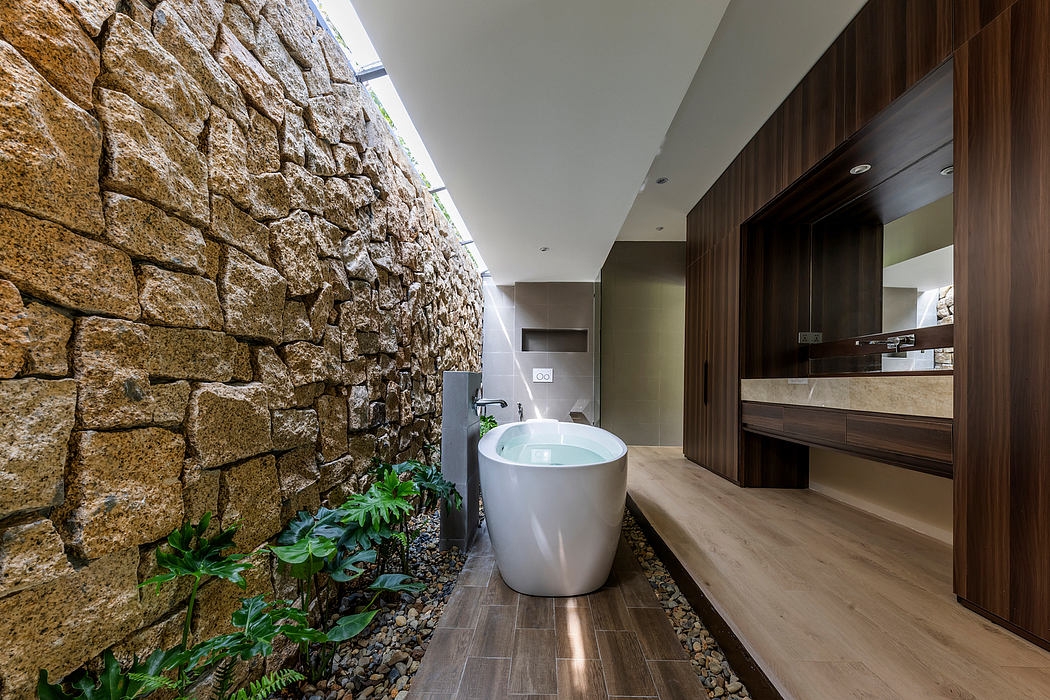 Striking stone wall, modern freestanding tub, and sleek wood cabinetry in this luxurious bathroom.