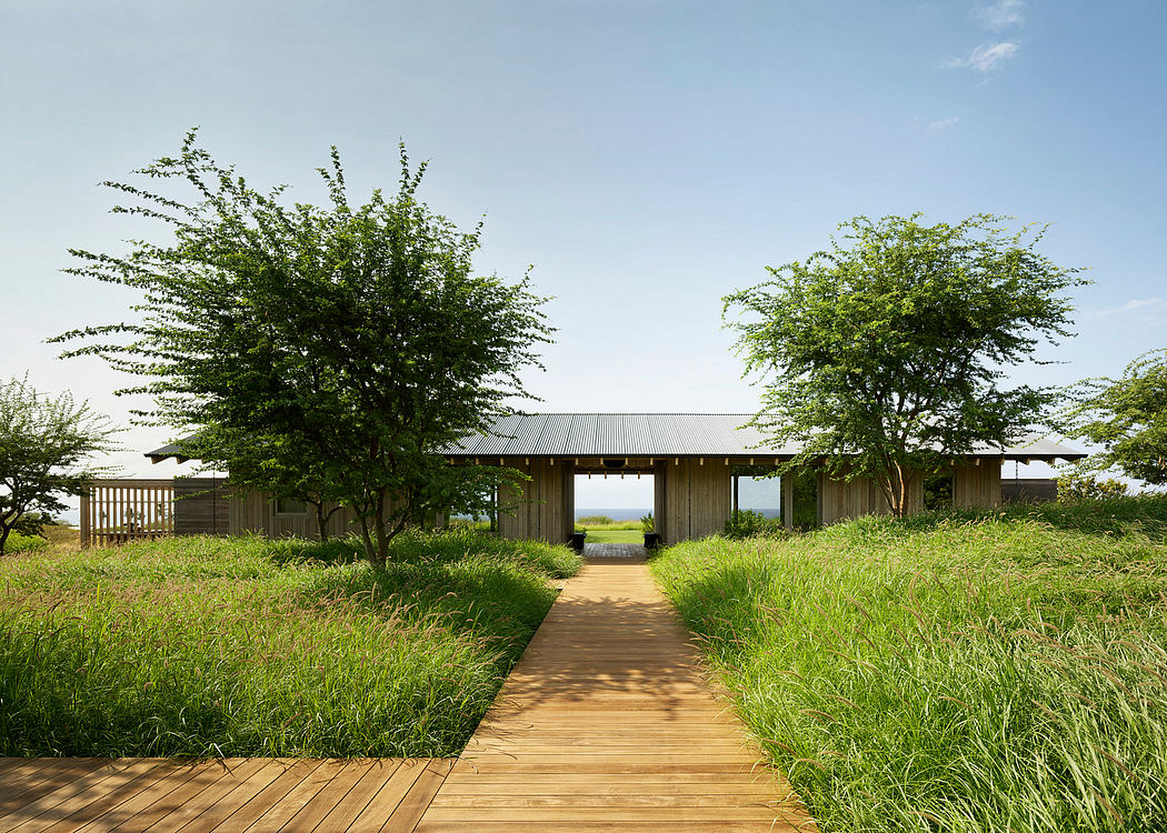 Wooden path leads to a modern, open-air structure surrounded by lush greenery.