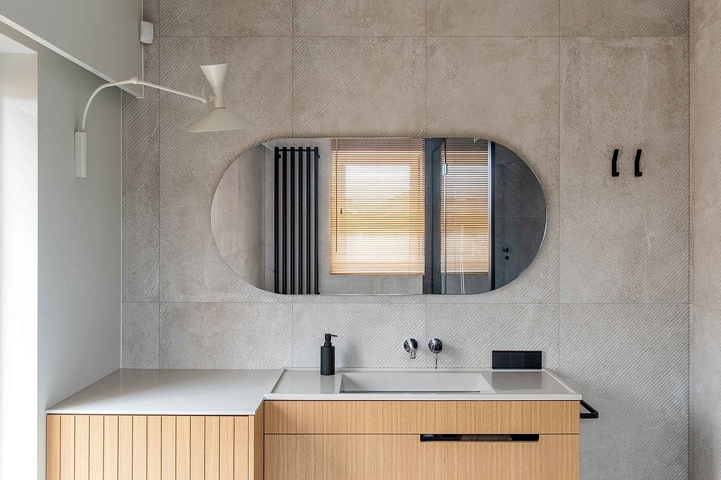 Minimalist bathroom design featuring wood vanity, oval mirror, and clean, sleek tiles.