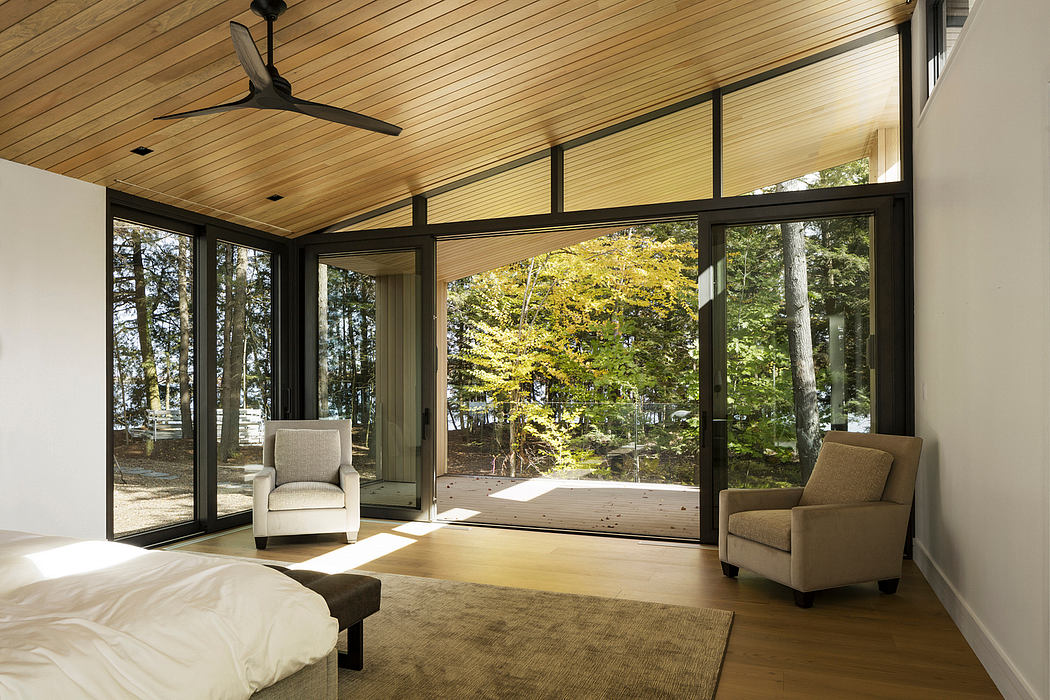 Cozy bedroom with expansive windows overlooking lush forest, warm wood tones, and modern furniture.
