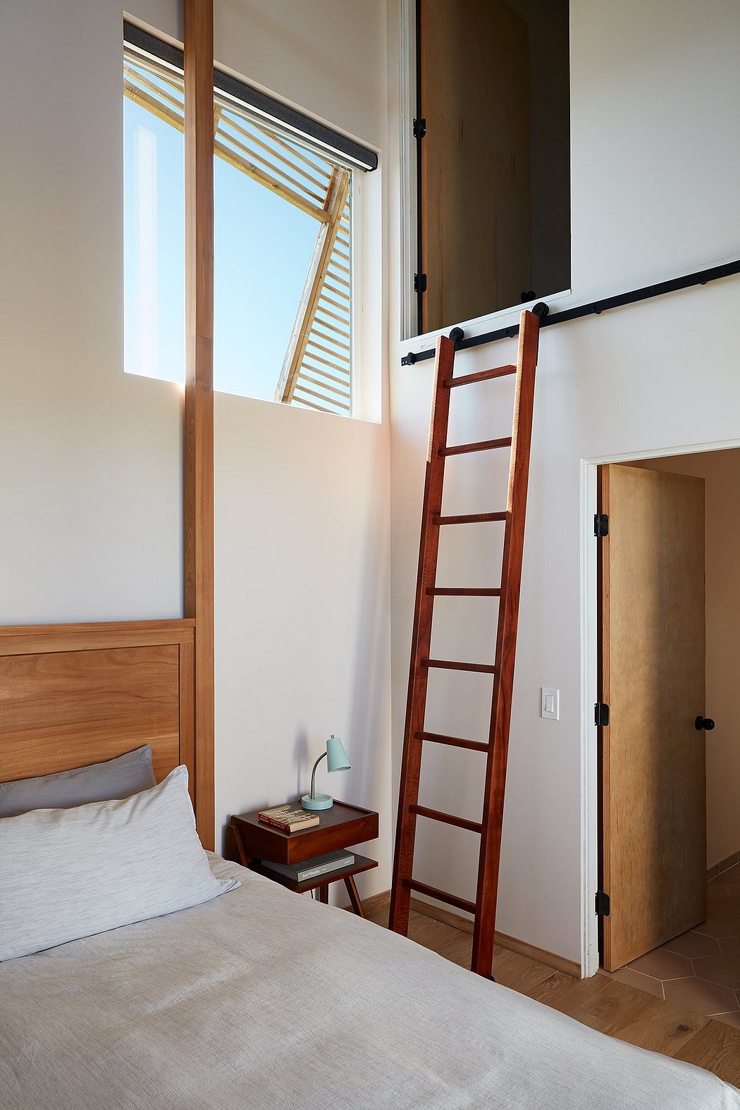 Minimalist bedroom with a wooden ladder and wooden furniture, framed by a large window.