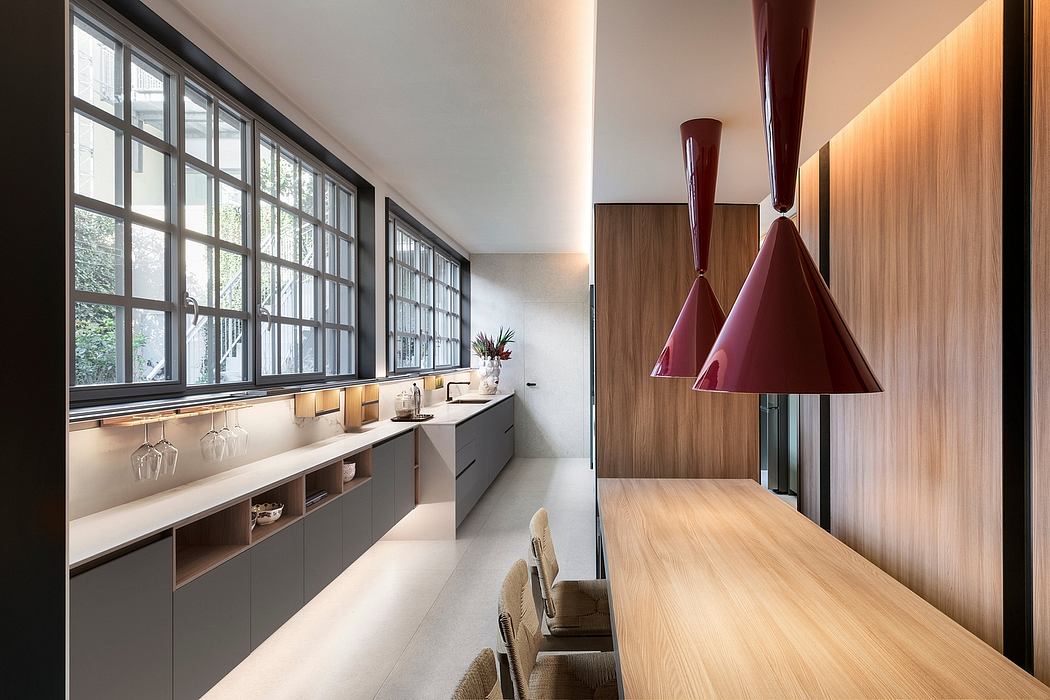 Modern kitchen with floor-to-ceiling windows, wooden cabinetry, and bold pendant lights.