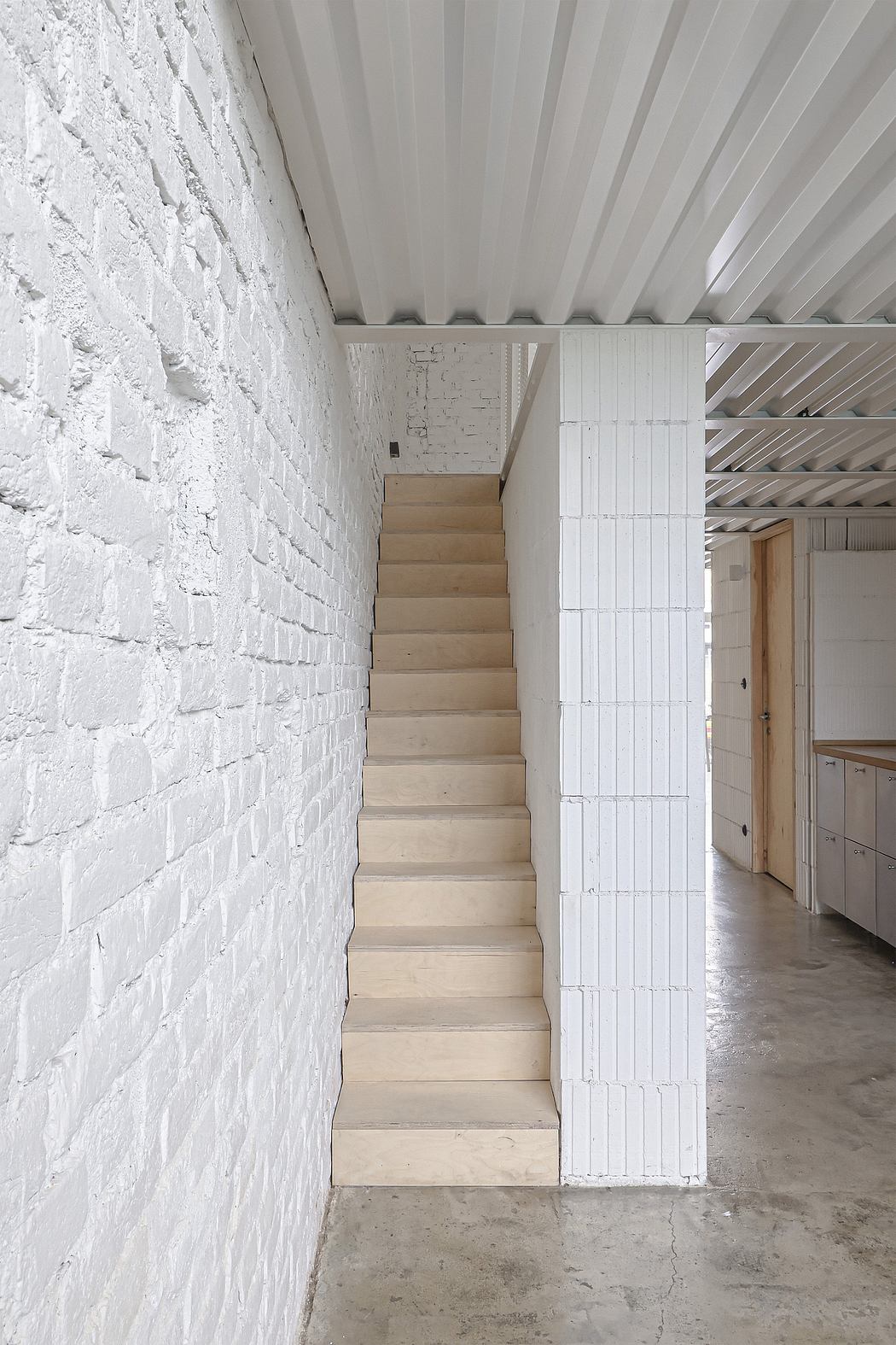 A modern staircase leading up against a textured white concrete wall and ceiling beams.
