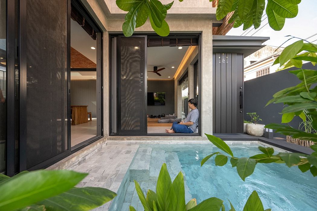 Sleek modern interior with a pool, lush greenery, and a person relaxing inside.