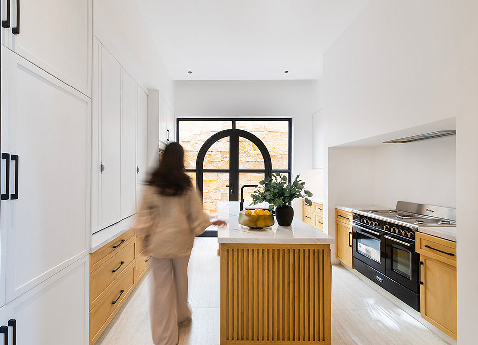 A modern kitchen with wood cabinetry, a large central island, and a striking arched window.