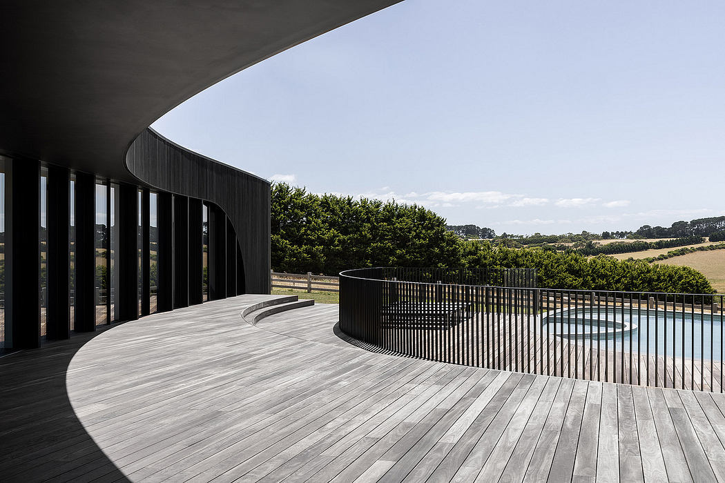 Curved, glass-walled structure with a wooden deck overlooking a pastoral landscape.