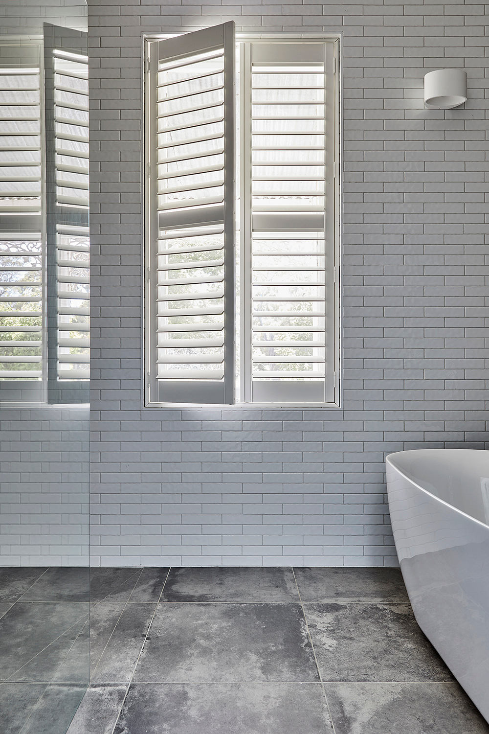 Bright, modern bathroom with sleek shuttered windows, clean tile flooring, and freestanding tub.