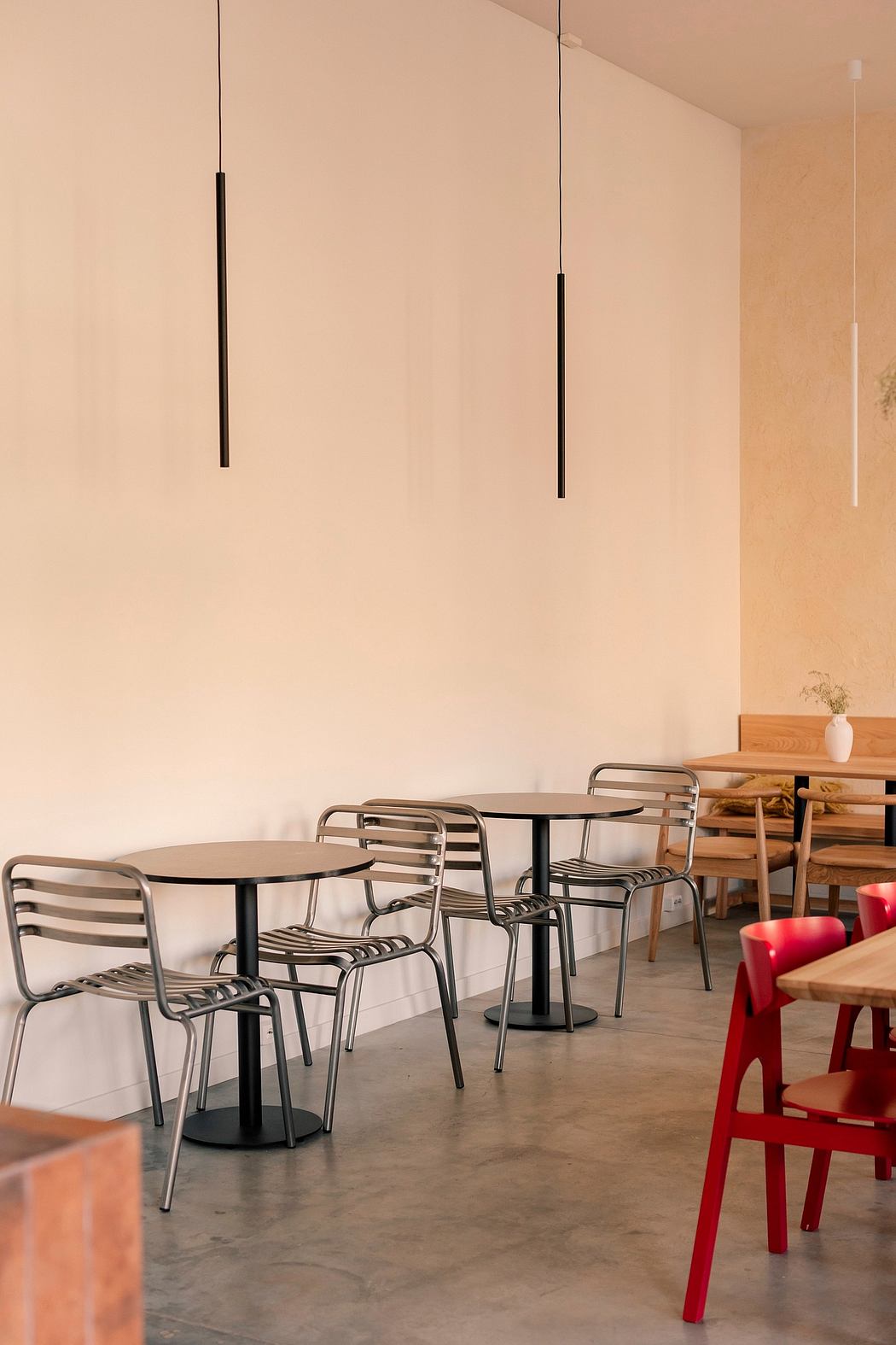 Modern cafe interior with minimalist tables, chairs, and pendant lighting against a warm-toned wall.