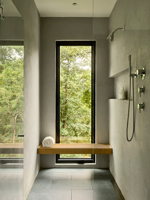 Modern bathroom with a large window overlooking lush greenery and a wooden bench.