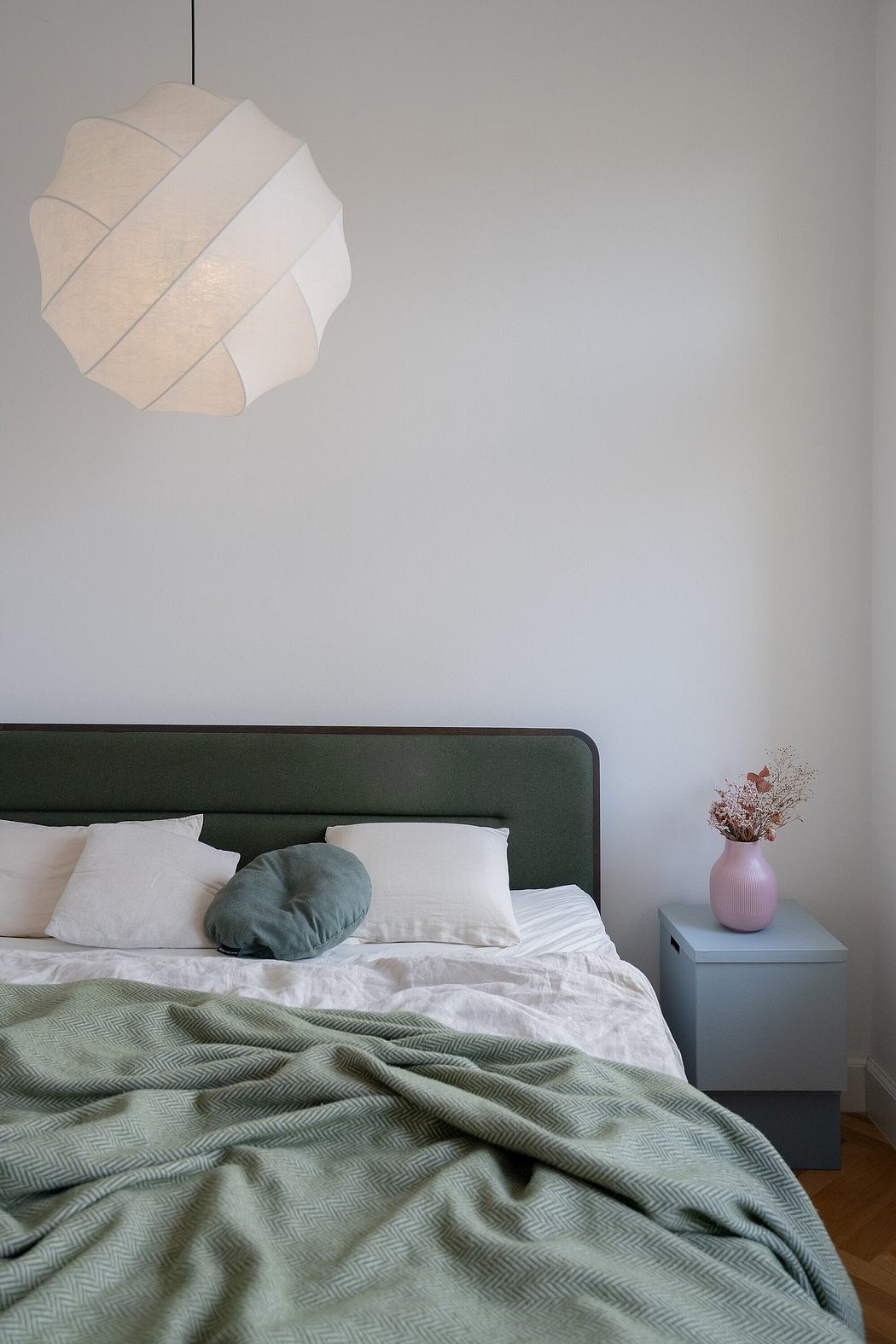 A modern bedroom with a plush green blanket, white bedding, and a striking pendant light.