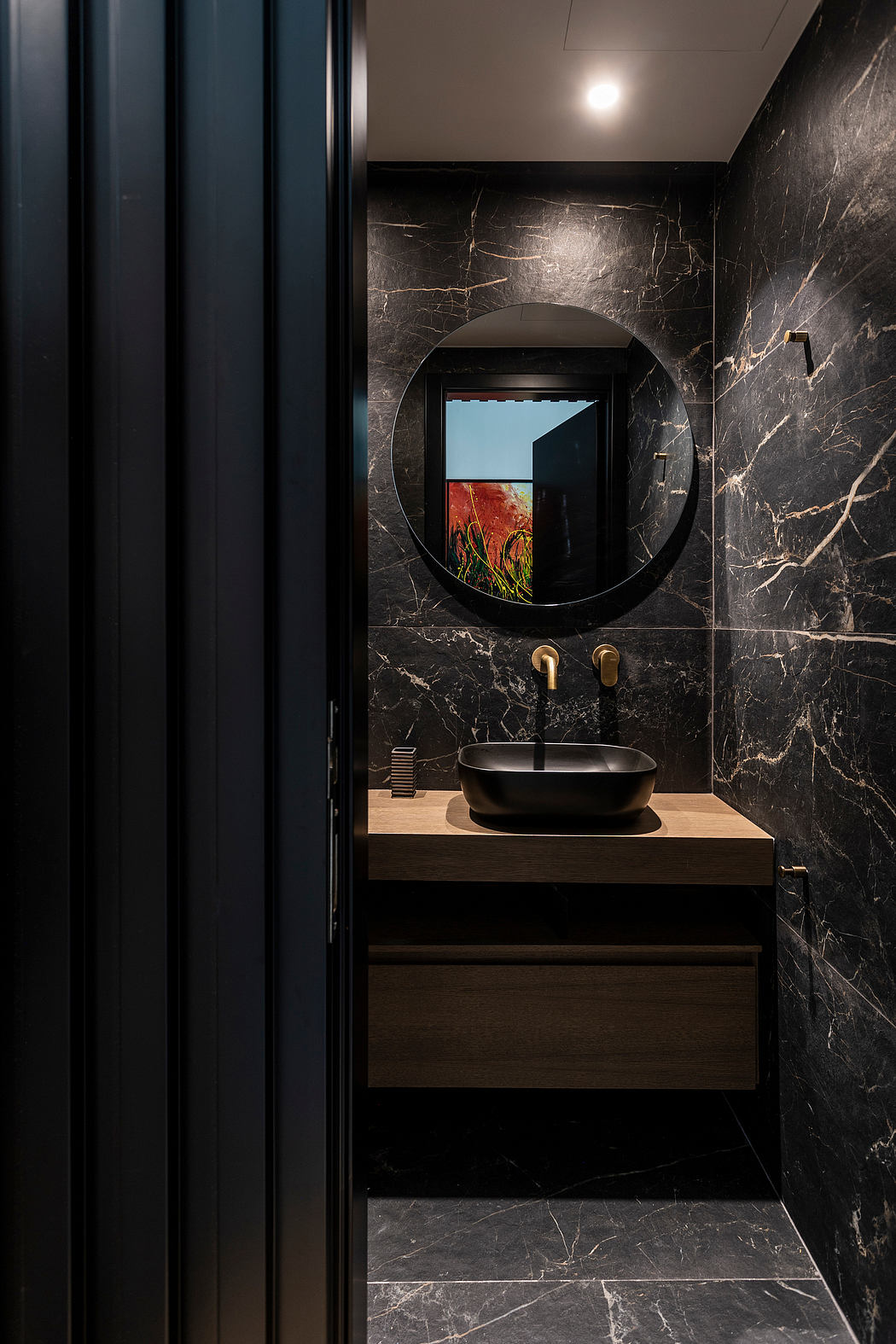 Sleek, modern powder room with dark marble walls, circular mirror, and wood vanity.