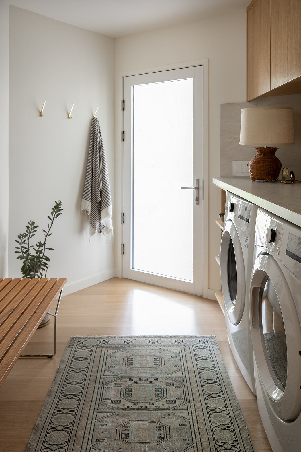 Cozy laundry room with wooden bench, rug, and modern washer-dryer in bright, minimalist space.