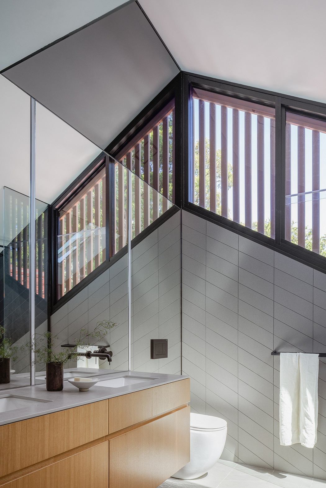 Geometric bathroom design with black frame windows, wood cabinetry, and gray tile walls.