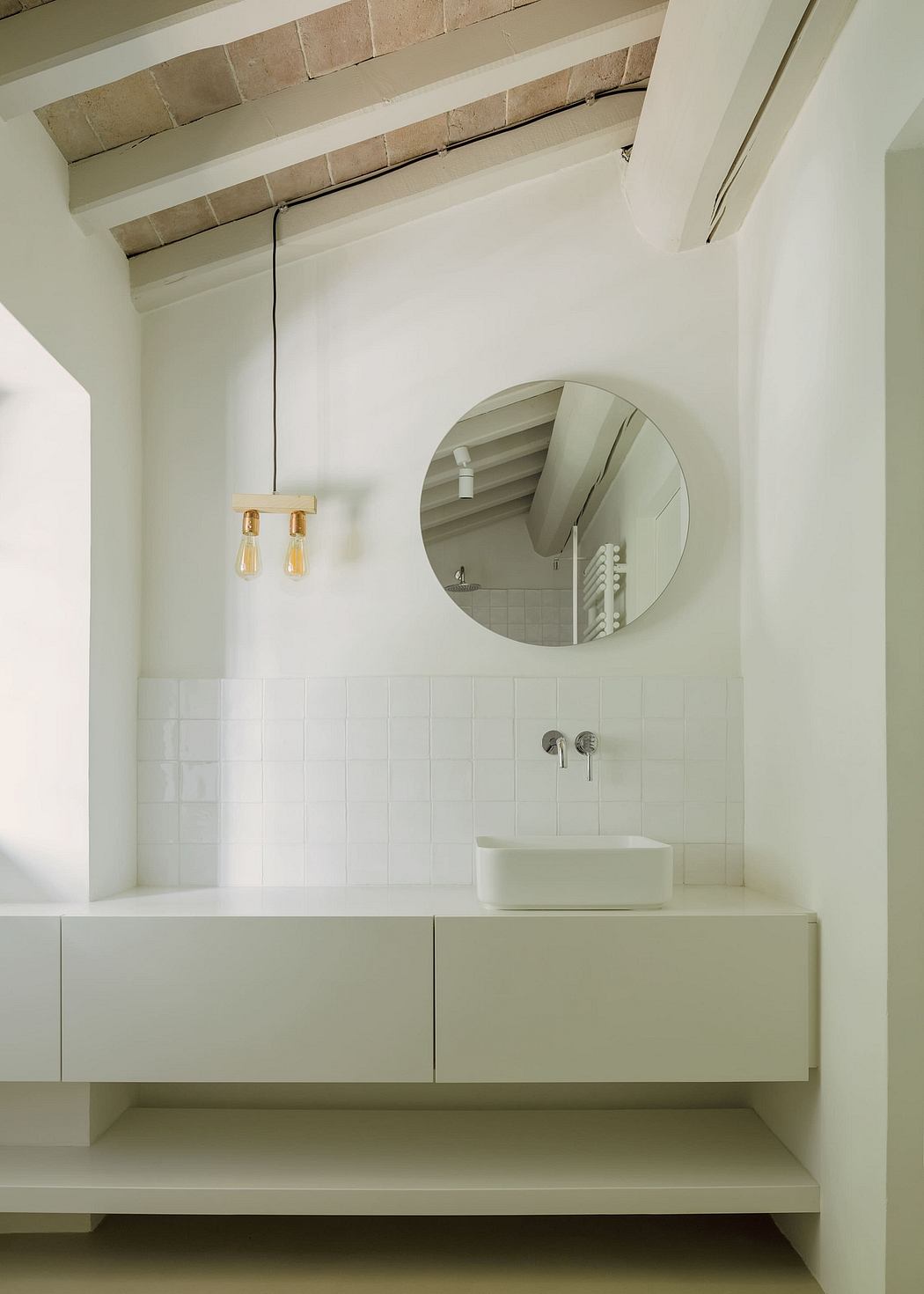 A minimalist bathroom with a round mirror, modern vanity, and textured ceiling beams.