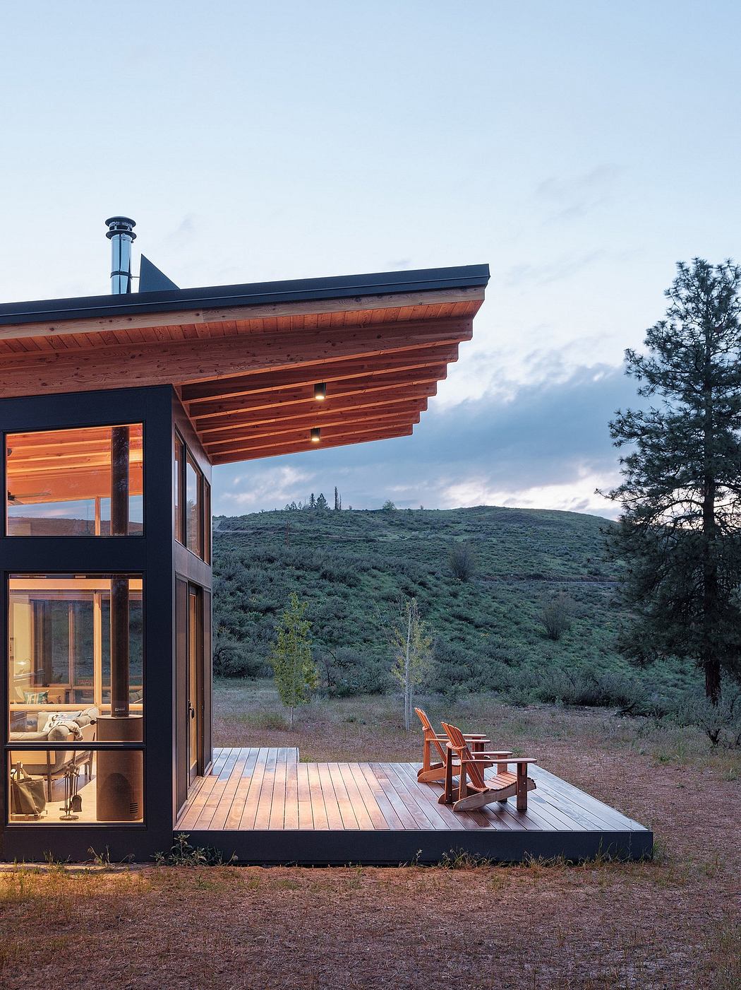 Rustic cabin with wooden roof, deck, and mountain landscape in the background.