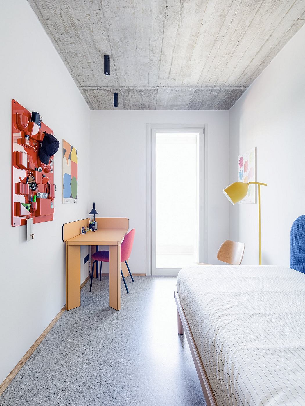 Minimalist bedroom with concrete ceiling, colorful accents, and a desk setup.