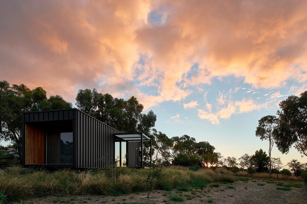 A modern, minimalist building with a striking black exterior and wooden accents, set against a vibrant sunset sky.