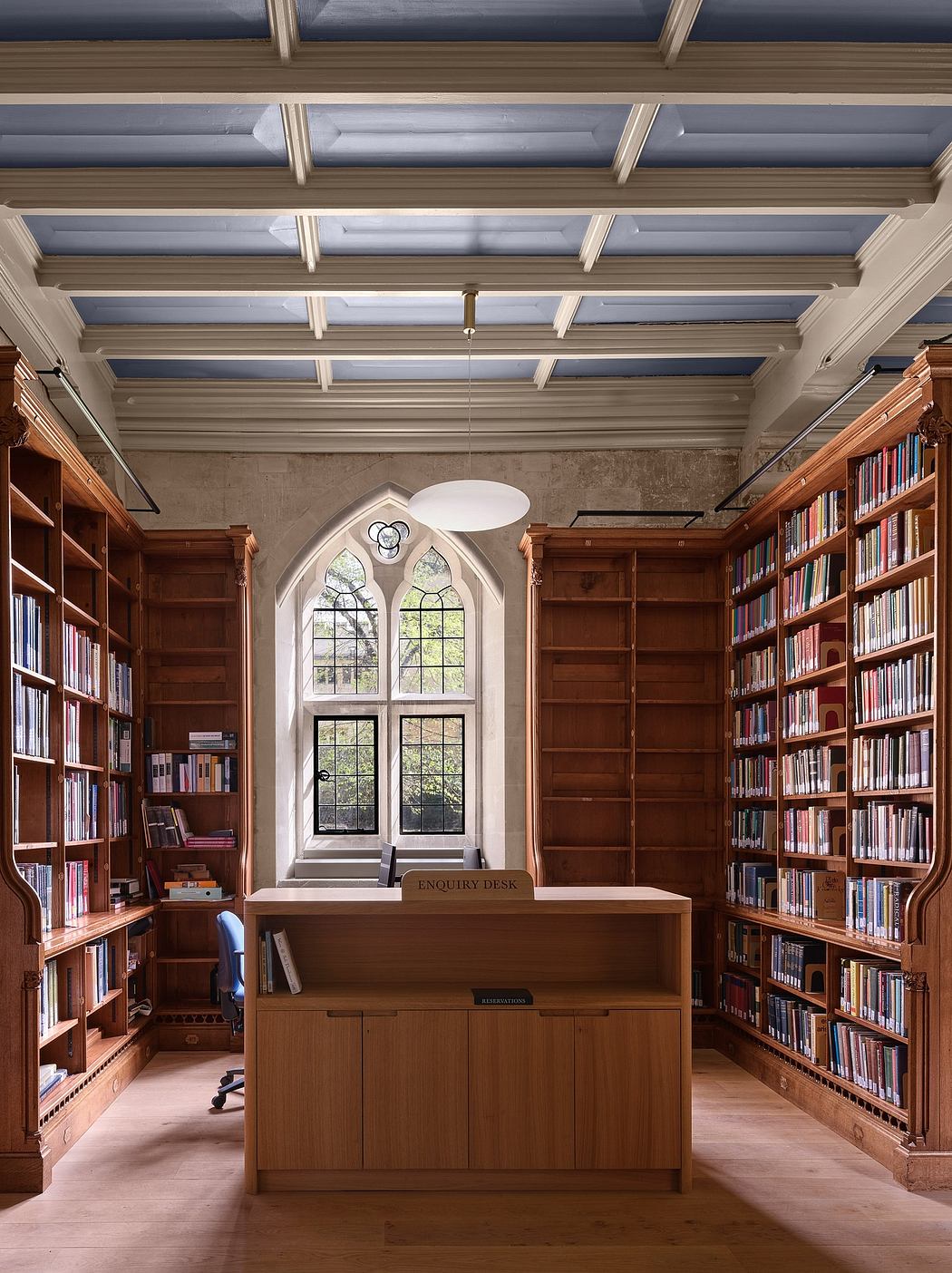 Ornate wooden bookshelves, arched windows, and an antique enquiry desk in a grand library.