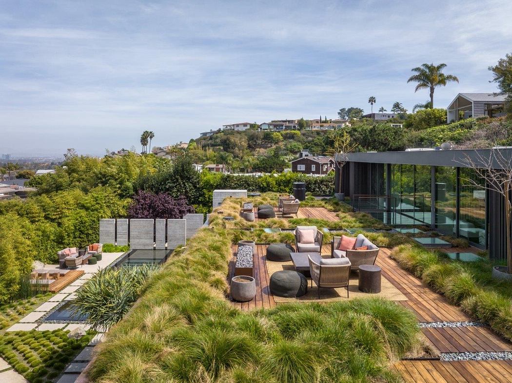 Expansive patio with lush greenery, contemporary seating, and glass-walled structure.