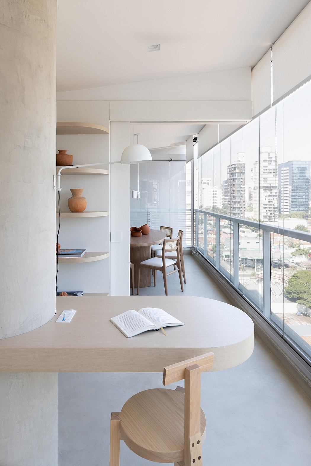 Minimalist apartment interior with wooden dining table, shelves, and full-length windows.