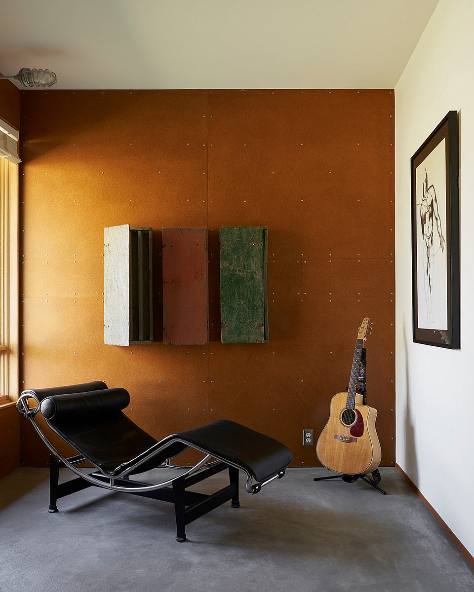 Minimalist living room with a lounger, guitar, and artwork on a textured wall.