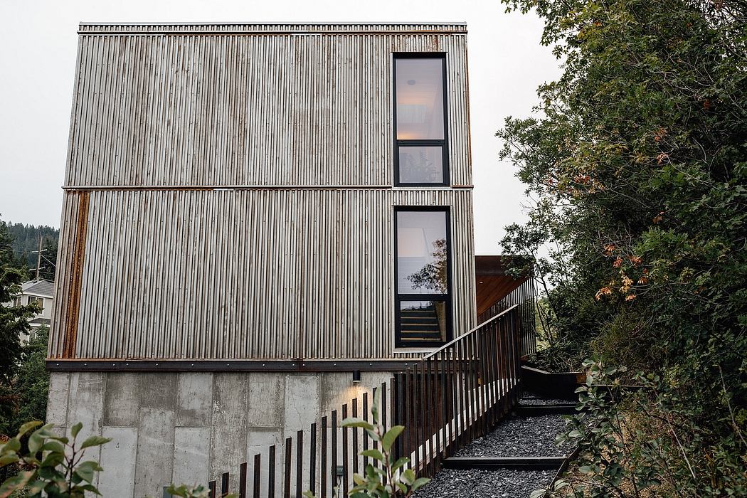A modern, minimalist building with a striking metal facade, large windows, and a wooden staircase.