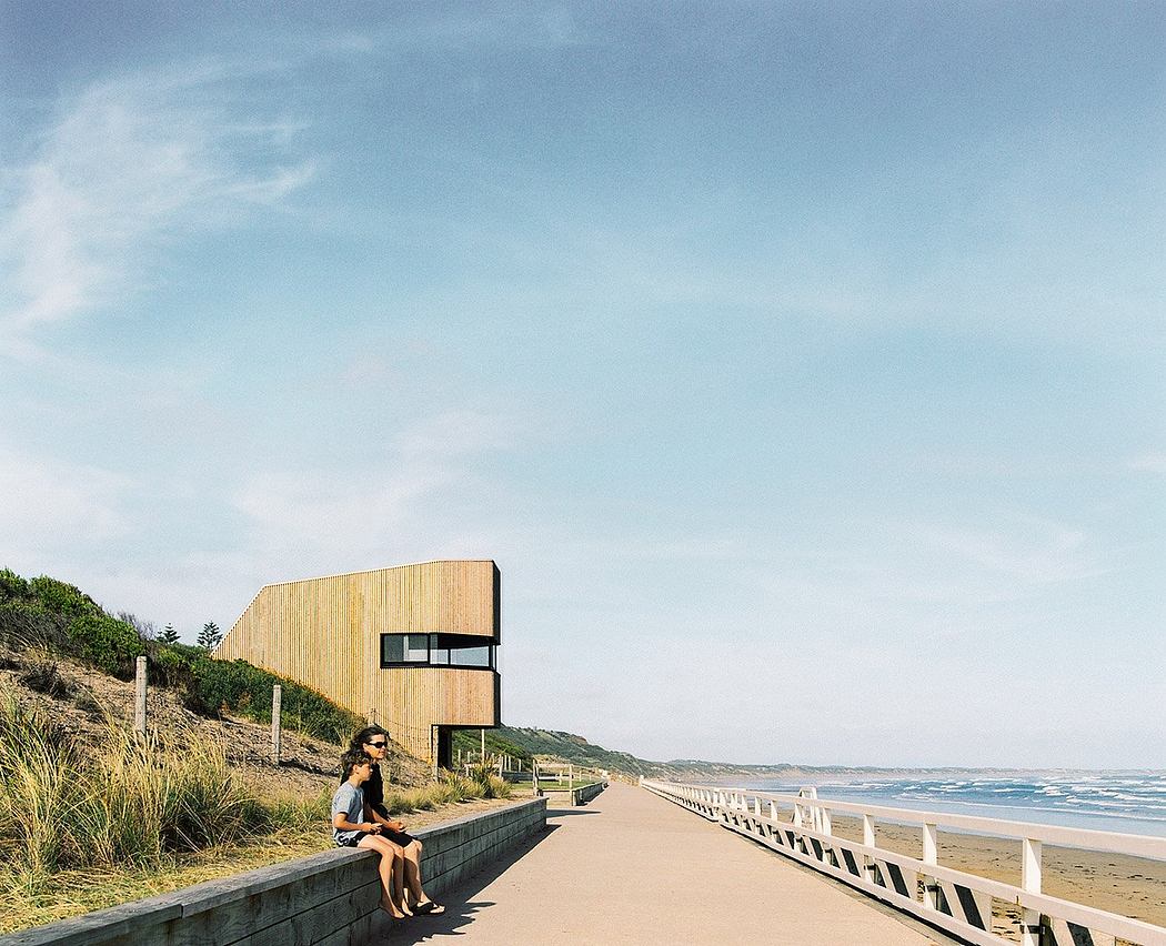 A modern wooden structure overlooking a coastal pathway and sandy beach.