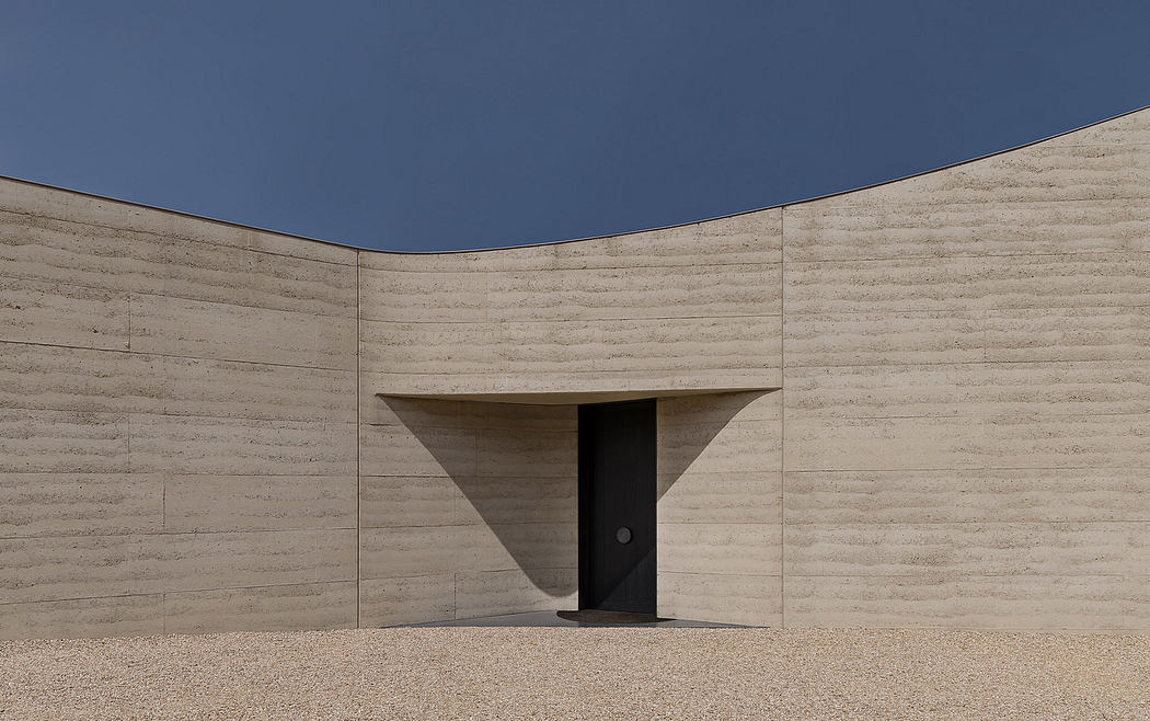 Minimalist, sculptural concrete structure with recessed entryway and stark contrasts.