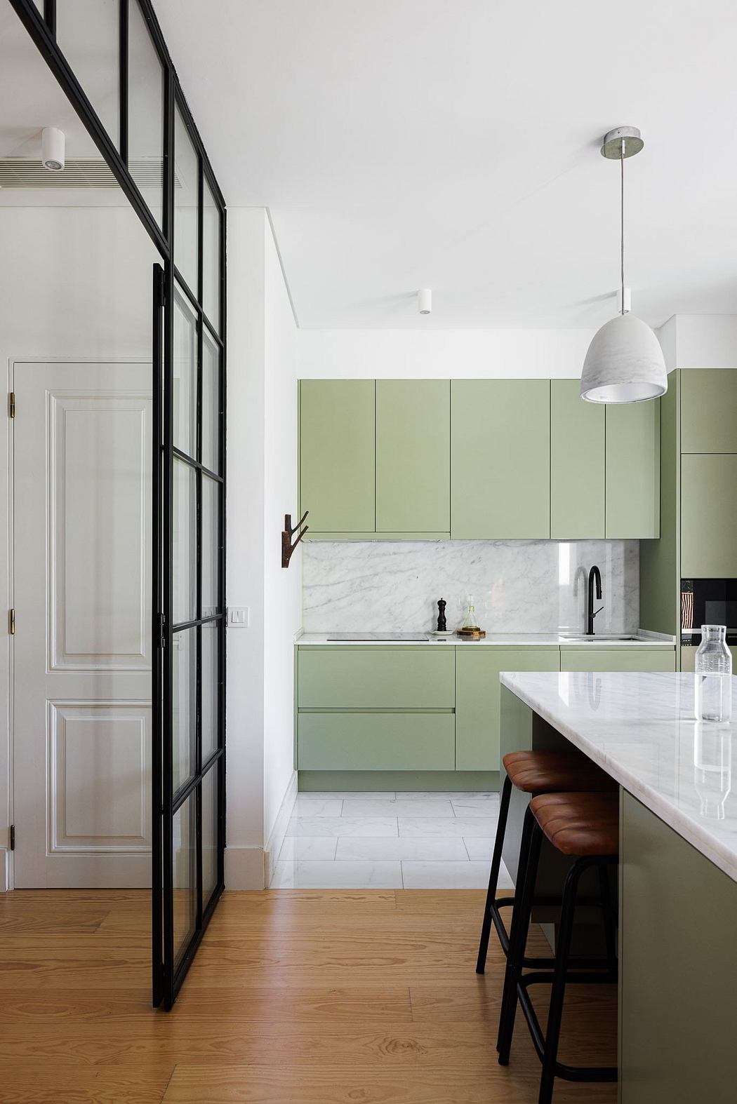 Elegant kitchen with sleek green cabinetry, marble countertops, and striking black-framed windows.