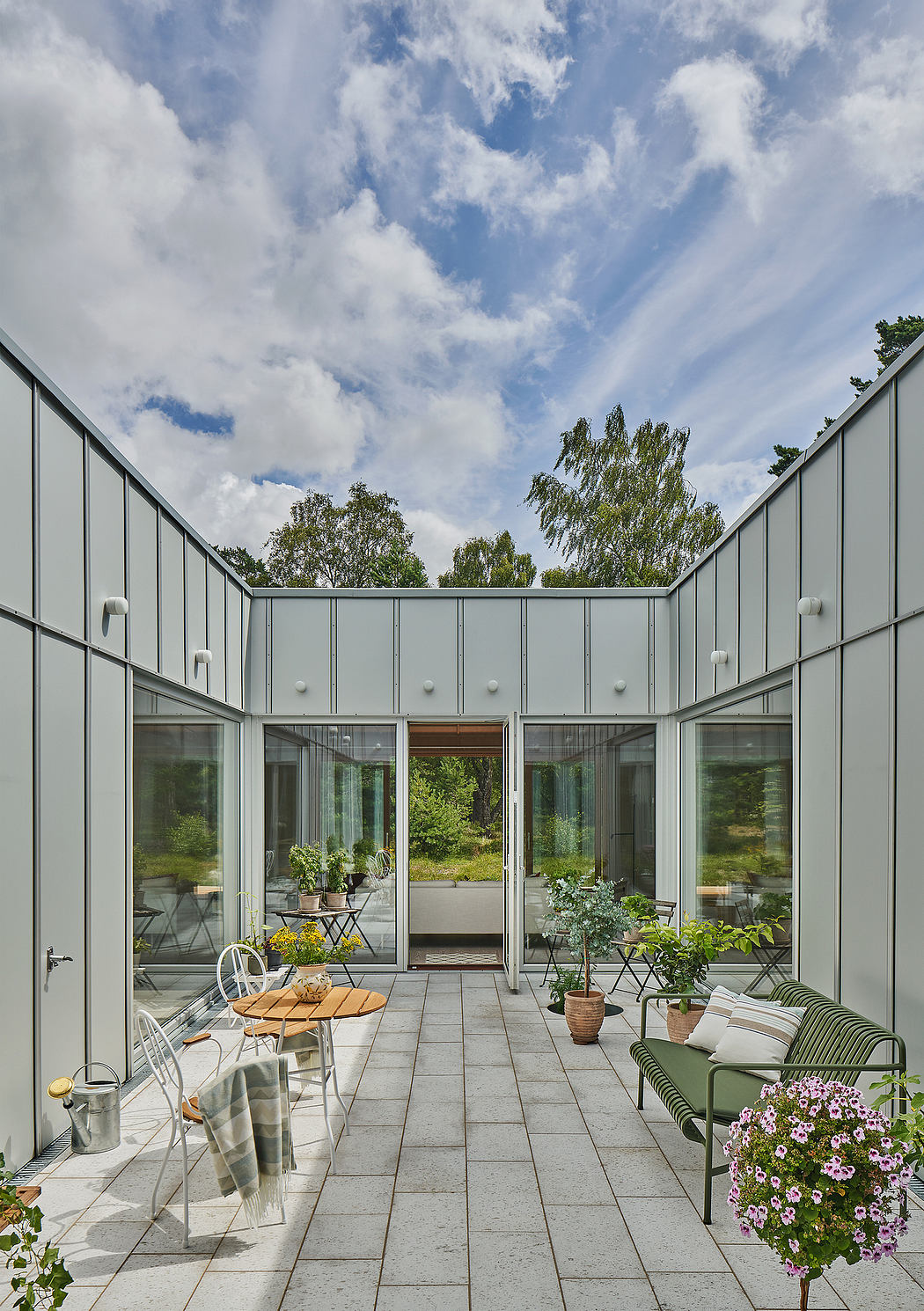 Minimalist outdoor terrace with sleek gray siding, glass walls, and mixed furniture.