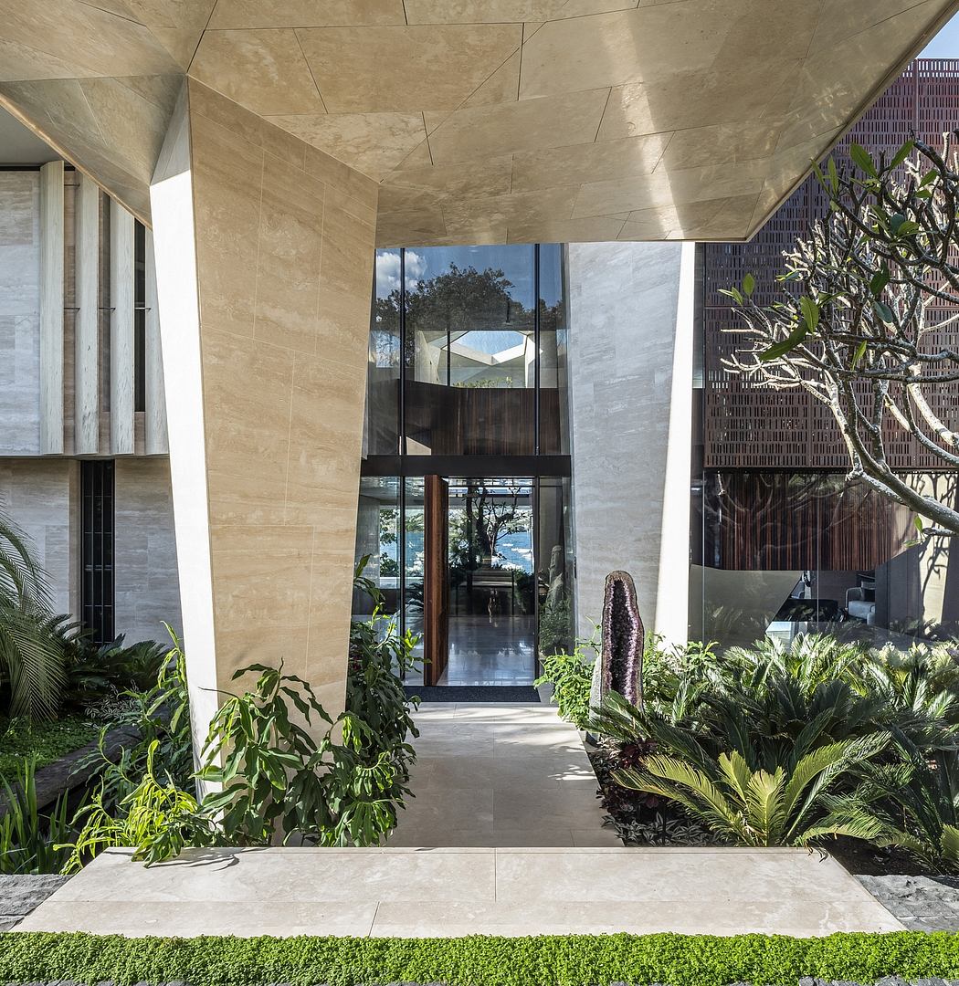 A modern, sleek entrance with a glass facade and lush tropical greenery surrounding it.