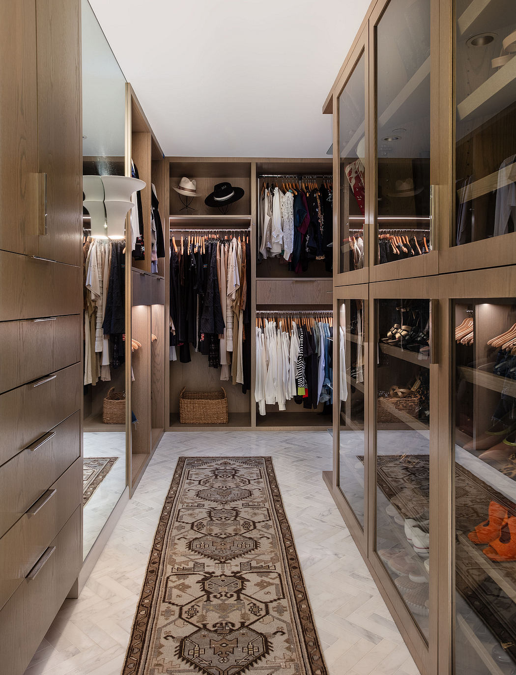 A spacious, organized walk-in closet with wooden cabinetry, ample hanging space, and a patterned rug.