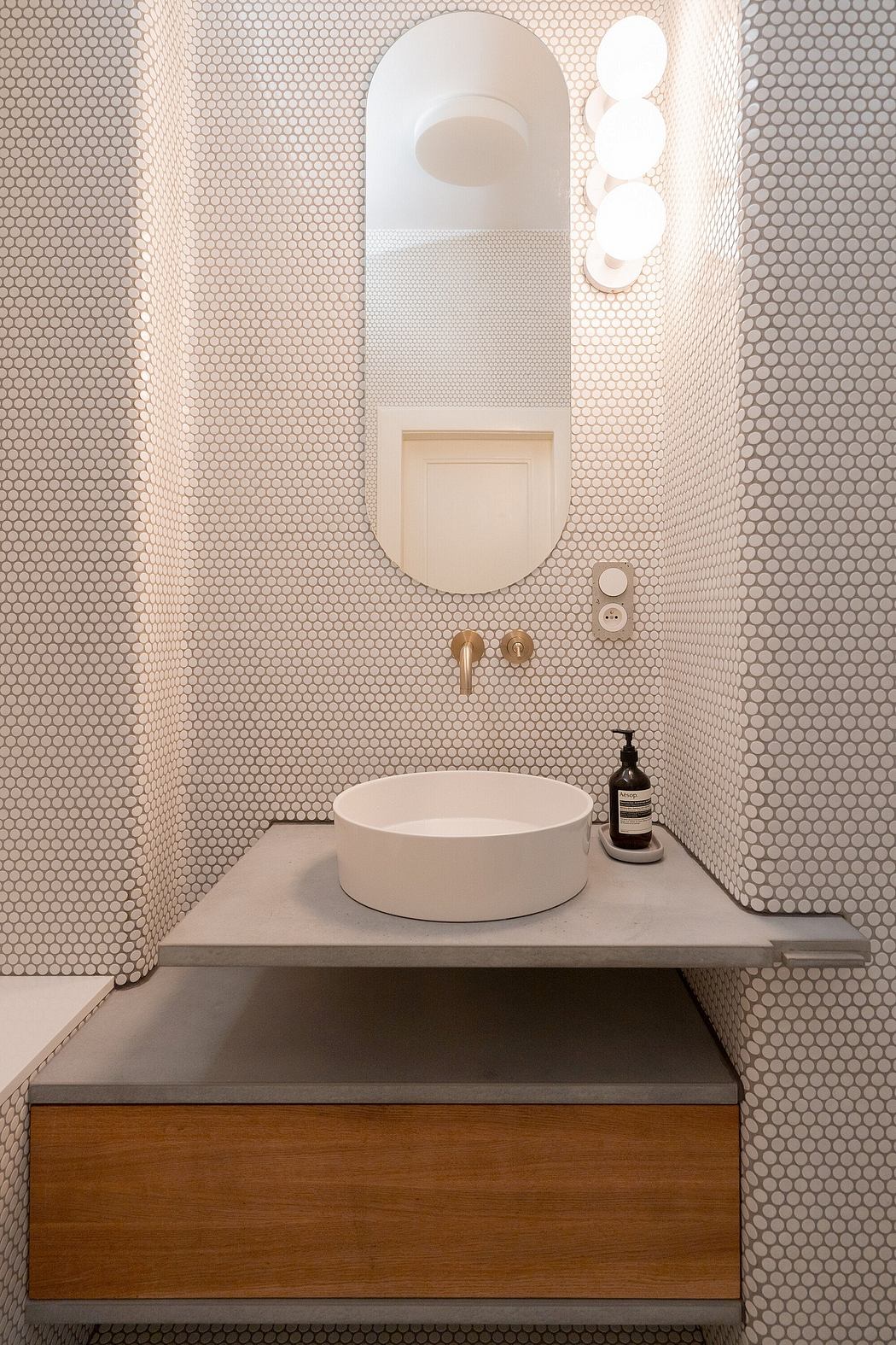 A modern bathroom with a sleek white circular sink, hex-patterned tile walls, and wood vanity.