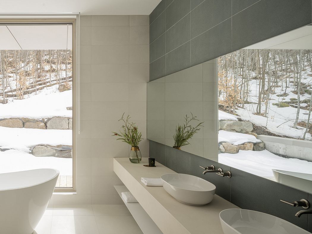 Minimalist bathroom with large window overlooking snowy landscape. Neutral tiles, vessel sinks.