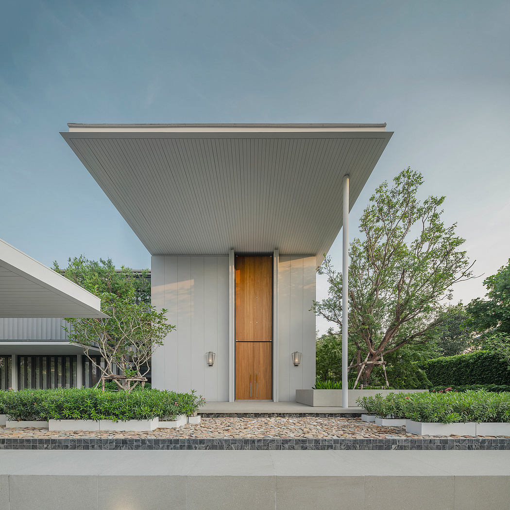 A modern, minimalist entryway with a wooden door, metal paneling, and lush greenery.