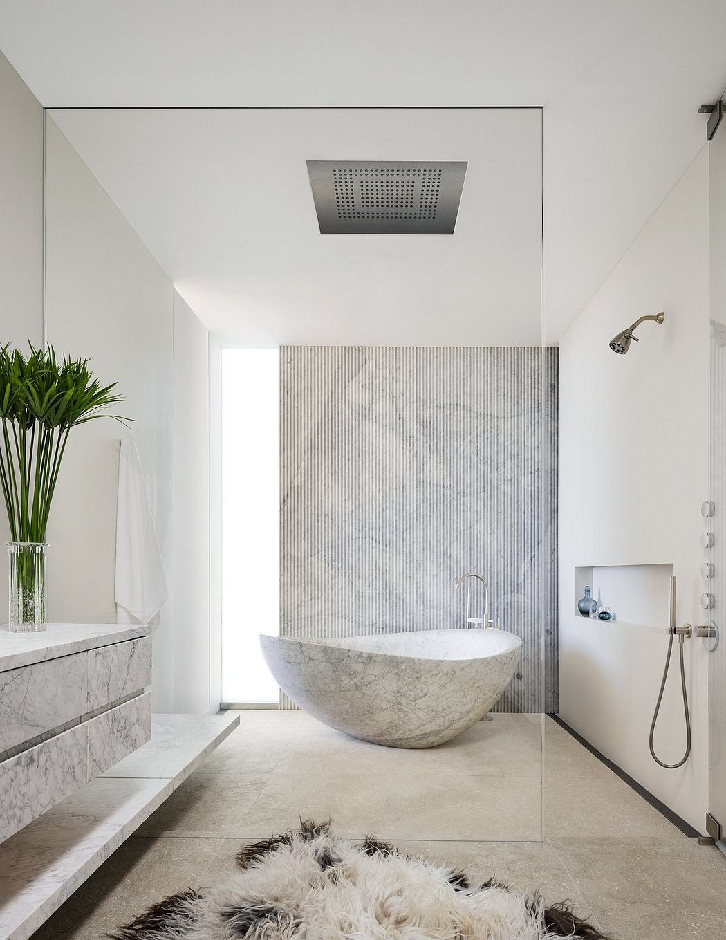 Minimalist bathroom with a freestanding stone bathtub, rainfall shower head, and marble vanity.