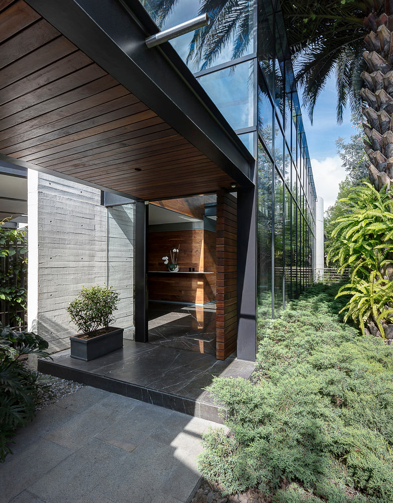 Modern glass-and-wood structure surrounded by lush greenery, featuring a sleek entryway.