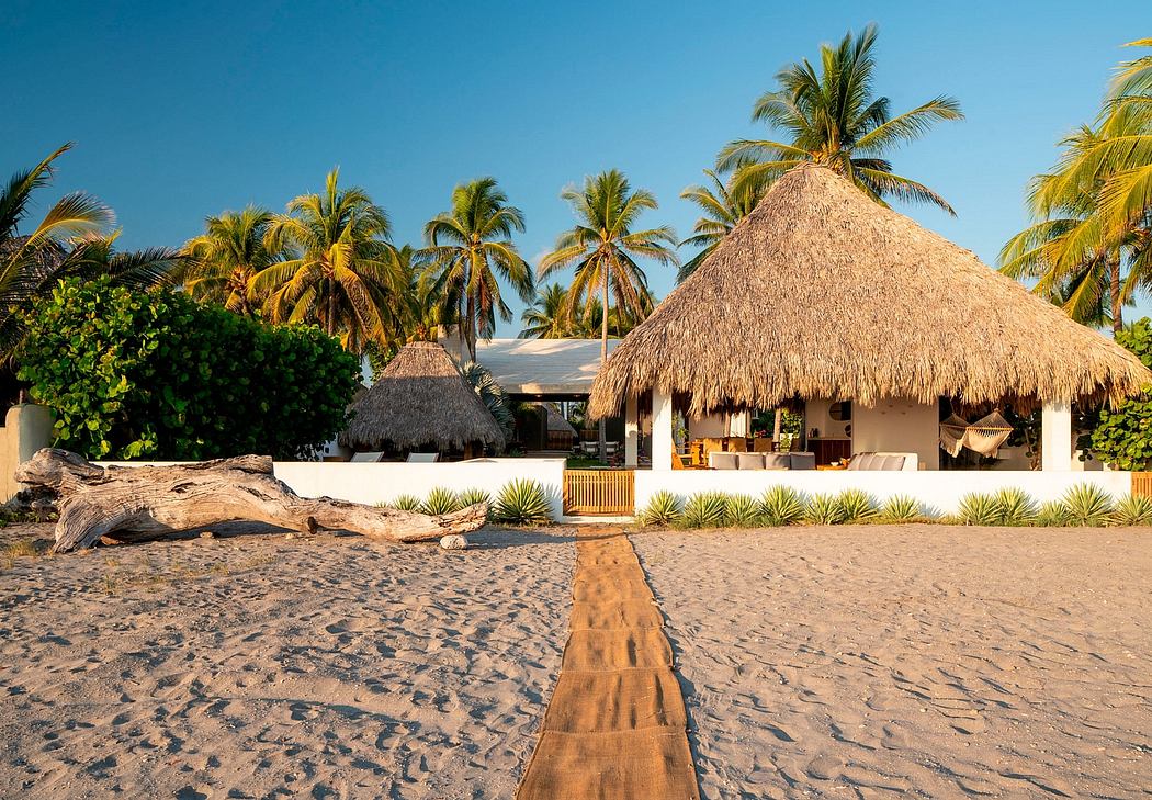 Beach resort with thatched-roof cabanas, palm trees, and sandy walkway leading to the shore.