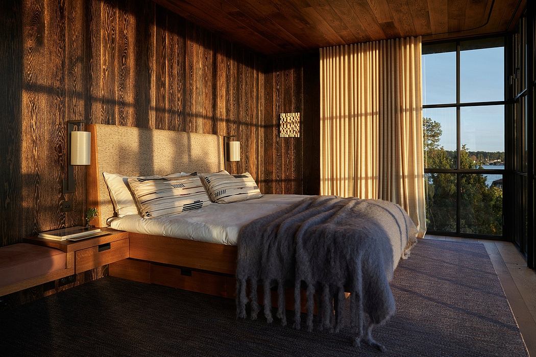 A cozy, rustic bedroom with wooden walls, a large bed, and floor-to-ceiling windows overlooking the outdoors.