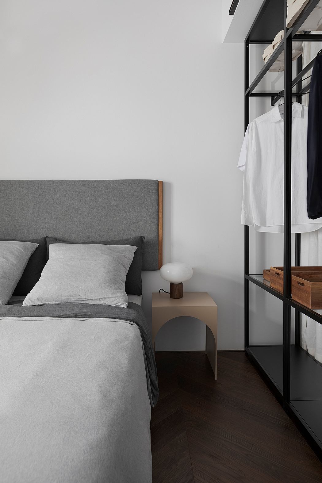 Minimalist bedroom with gray upholstered headboard, wood-tone bedside table, and open metal shelving.
