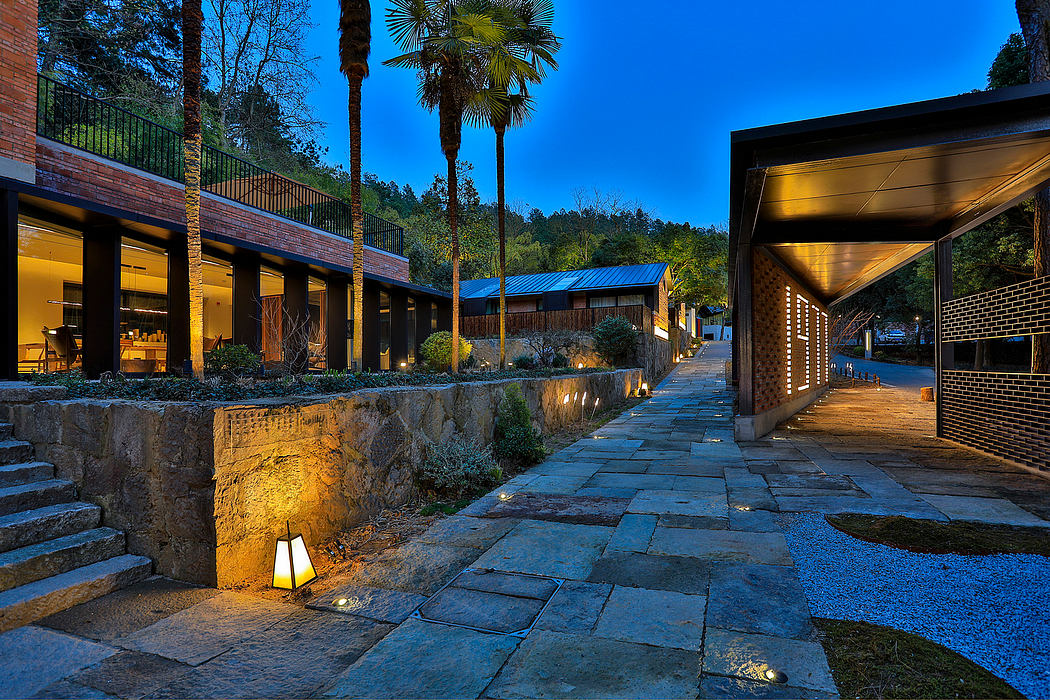 A tranquil outdoor walkway lined with brick buildings, palm trees, and illuminated stone steps.