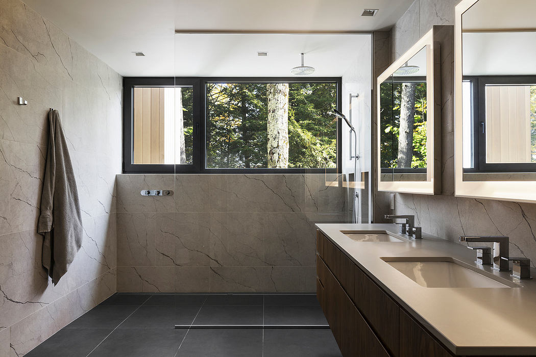 Sleek, modern bathroom with large windows offering scenic forest views, neutral tones, and minimalist design.