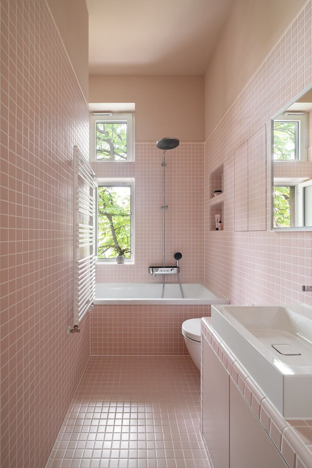 Sleek, pink-tiled bathroom with a bathtub, shower, and large windows overlooking nature.